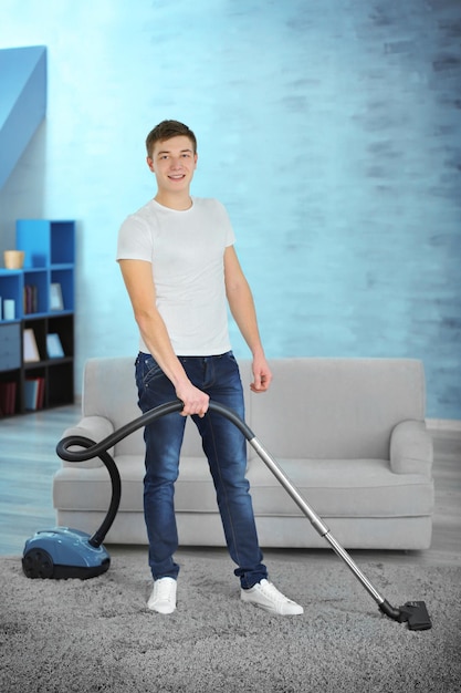 Young man with vacuum cleaner cleaning carpet at home