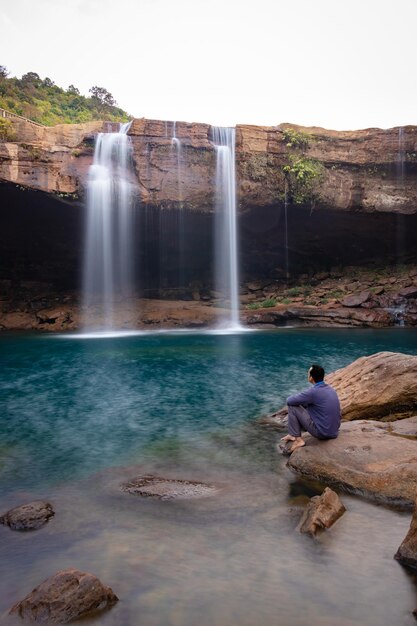 Young man with waterfall streams falling from mountain top at morning long exposure shot