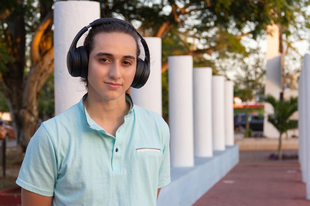 young man with wireless headphones looking at the camera in a park