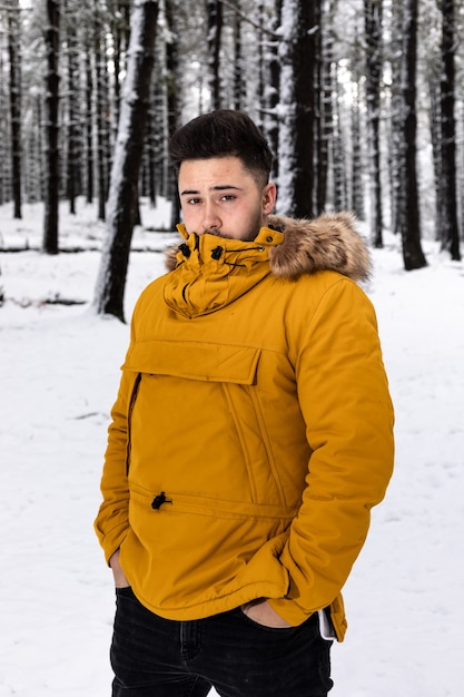 Giovane con una giacca a vento gialla in posa nel mezzo di un bosco innevato