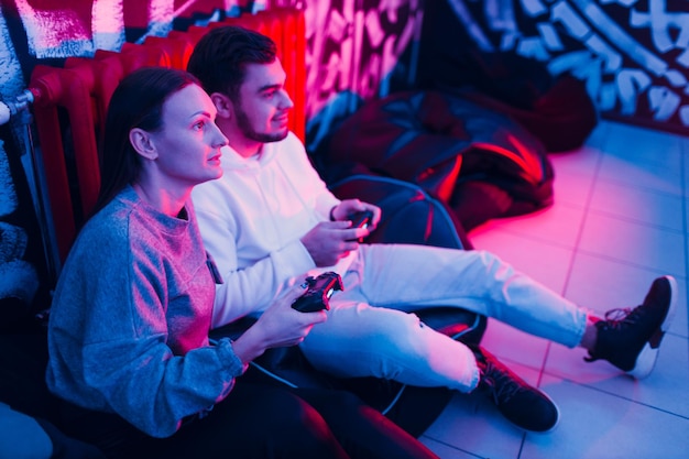 Young man and woman couple plays on game console with gamepad sitting on chair