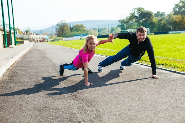 Young man and woman doing push-up exercise and touching the palms at the stadium