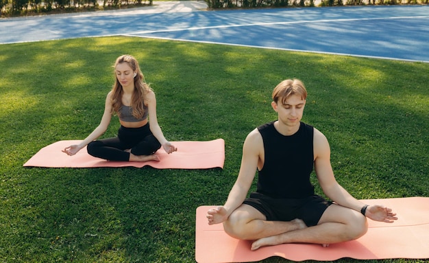 Young man and woman doing yoga in the sunny summer park Couples Yoga on green grass outdoor