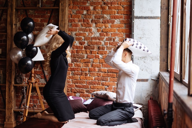 Photo a young man and a woman fight with pillows on a bed in a loft-style room