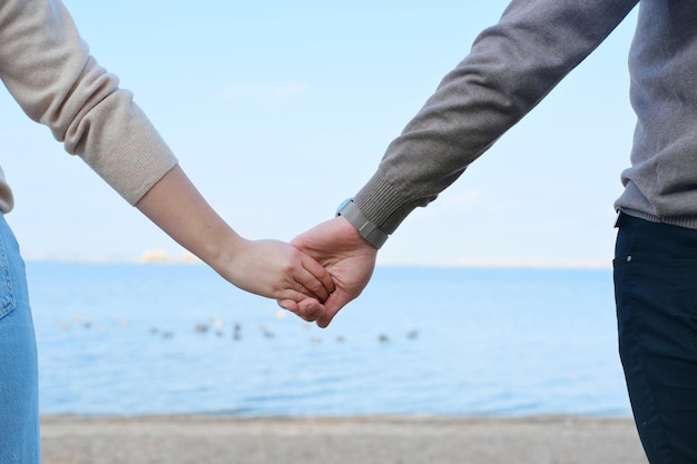 Young man and woman hold hands against the backdrop of blue water and sky Closeup of hands