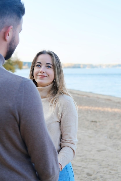 Young man and woman holding hands and posing on the beach The girl looks at the guy and smiles