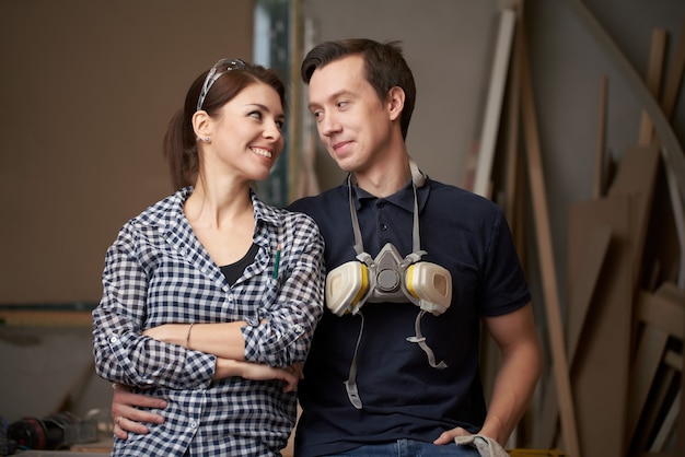 Young man and woman joiners sitting in workshop on background of boards