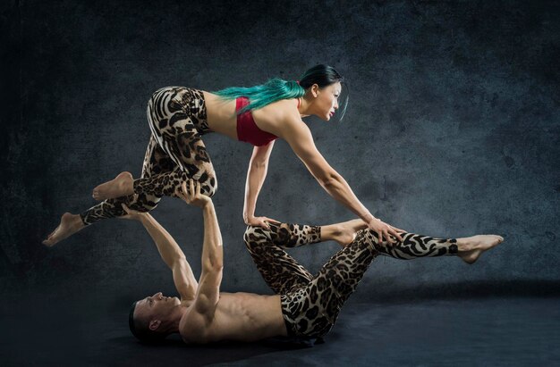 Young man and woman practicing acrobat against gray background