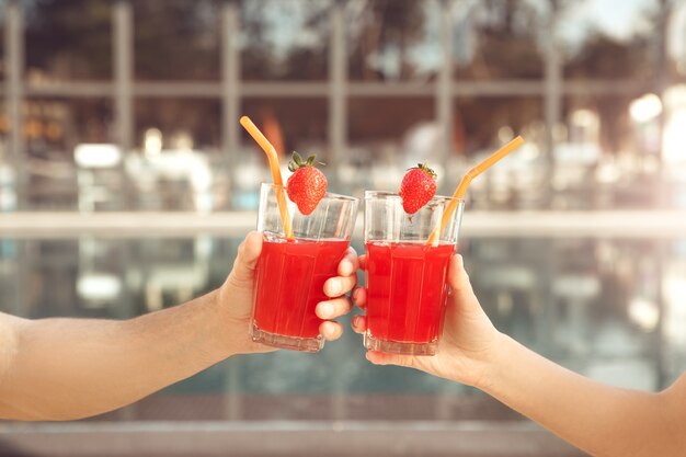 Young man and woman rest together near swimming pool drinking cocktail