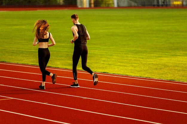 Young man and woman running on race track in stadium Young male and female athletes practicing toge