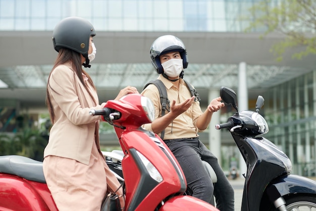 Young man and woman on scooters talking when standing in traffic jam and waiting fot green light