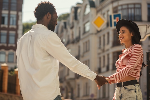 Foto giovane uomo e donna in piedi l'uno di fronte all'altro e tenendosi per mano mentre si sorridono l'un l'altro per strada