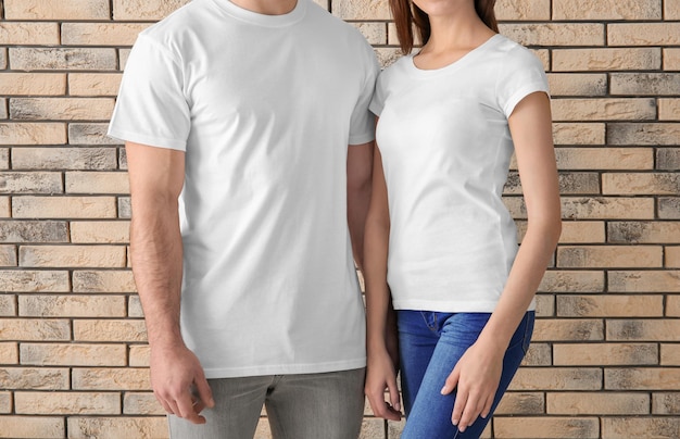 디자인을 위한 벽돌 벽 모형 근처의 세련된 흰색 티셔츠를 입은 젊은 남녀