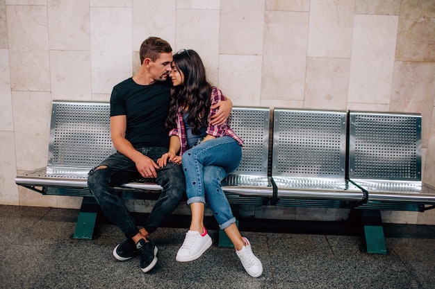 Young man and woman use underground. Couple in subway. Sitting on bench