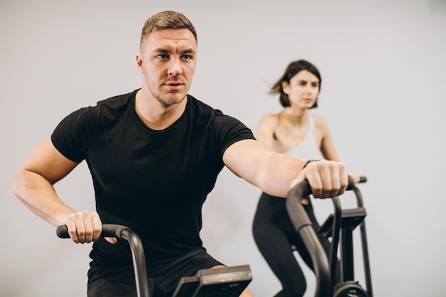 Young man and woman using air bike for cardio workout at cross training gym