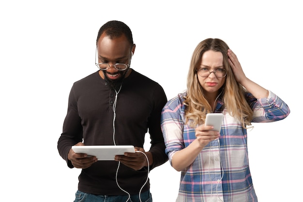 Giovane uomo e donna che utilizzano laptop, dispositivi, gadget isolati sul muro bianco. concetto di moderne tecnologie, tecnologia, emozioni, pubblicità. copyspace. acquisti, giochi, incontri di formazione online.