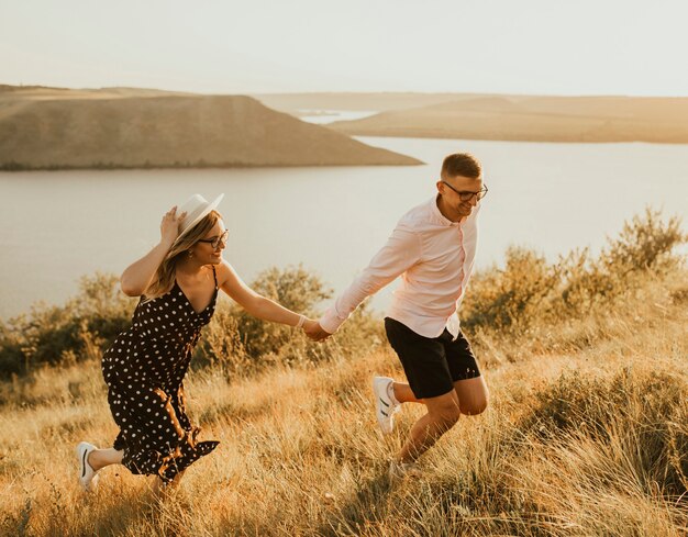 湖の近くの夏の日没時に牧草地を歩く若い男性と女性。