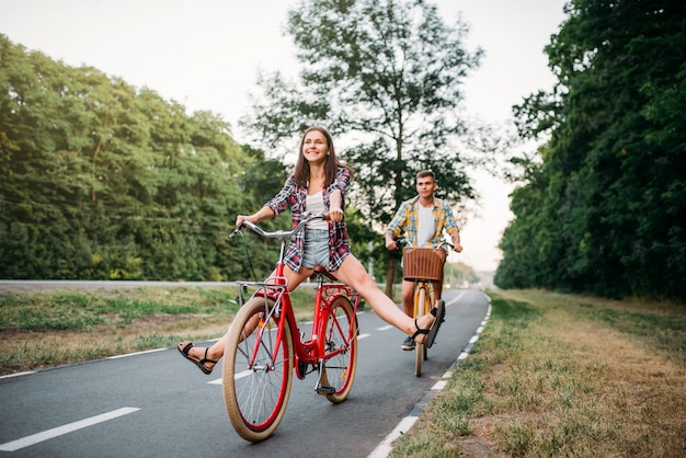 若い男性と女性がレトロなバイクの上を歩きます。ビンテージ自転車で幸せなカップル。古いサイクル、ロマンチックな旅