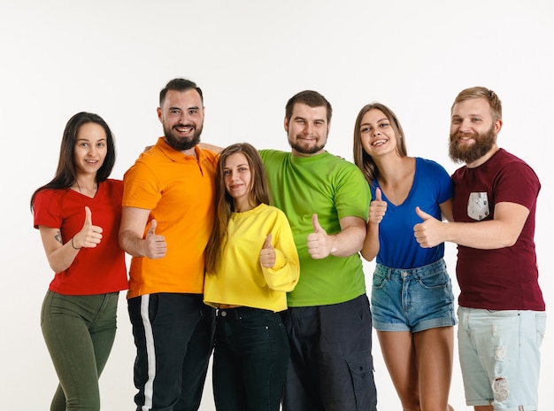 Young man and woman weared in LGBT flag colors on white wall. Caucasian models in bright shirts. Look happy, smiling and hugging. LGBT pride, human rights and choice concept.