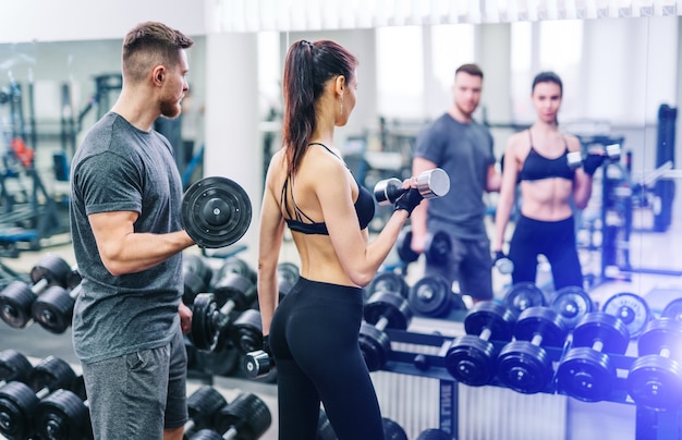 young man and woman with barbell flexing muscles in gym