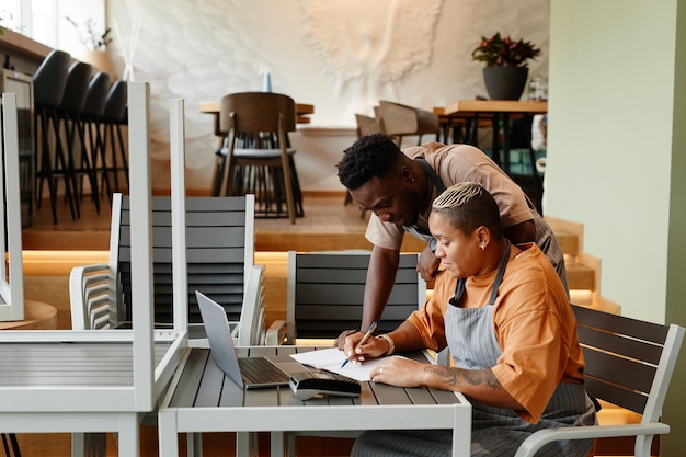 Young man and woman working together in modern cafe starting workday checking list of products for d...