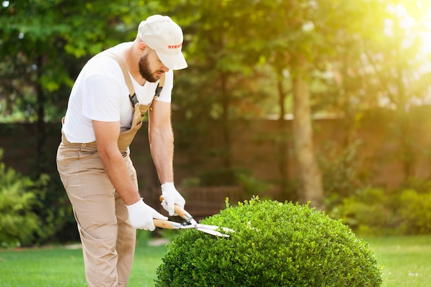 Young man worker in uniform at green garden