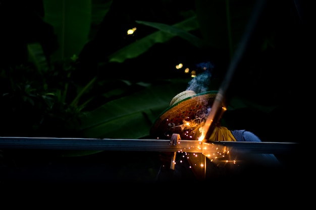 Young man worker welding iron pieces at work with protective goggles