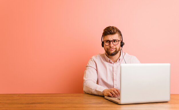 Young man working in a call center confused, feels doubtful and unsure