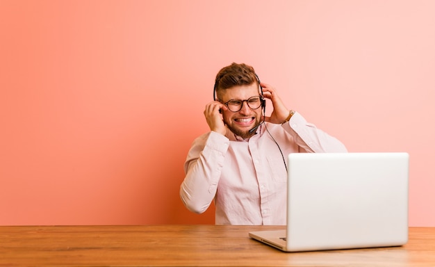 Young man working in a call center coning ears with his hands.