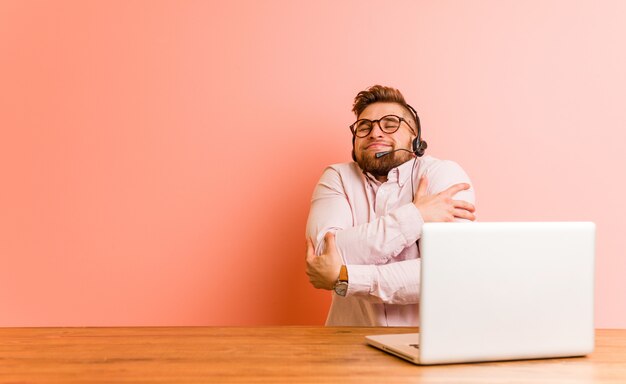 Young man working in a call center hugs himself, smiling carefree and happy.