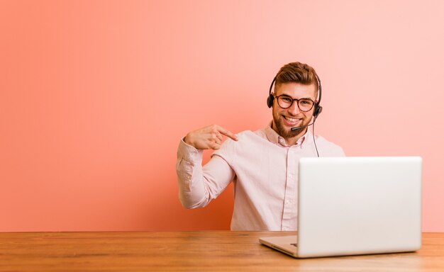 Young man working in a call center person pointing by hand to a shirt copy space, proud and confident