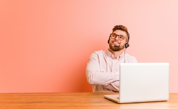 Young man working in a call center smiling confident with crossed arms.