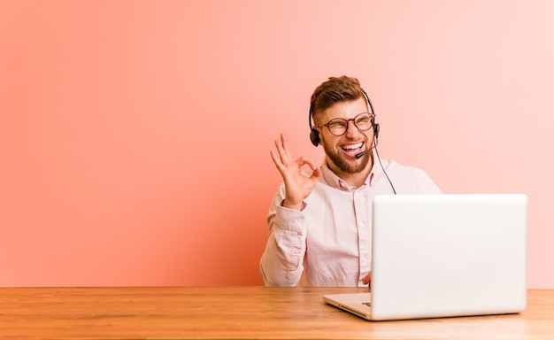 Young man working in a call center winks an eye and holds an okay gesture with hand.