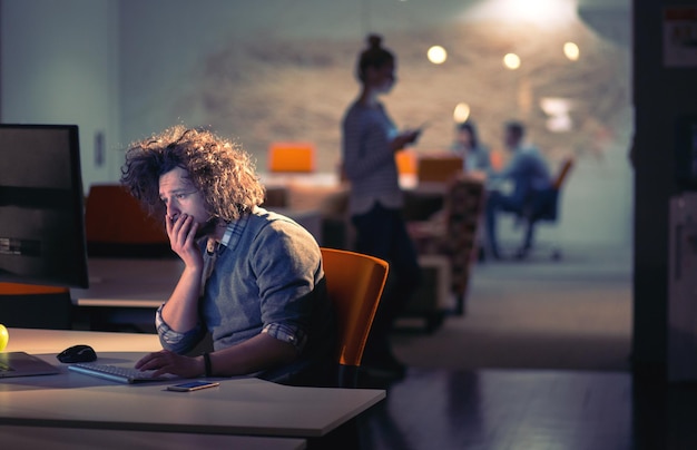 Young man working on computer at night in dark office. The designer works in the later time.