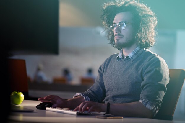 Young man working on computer at night in dark office. the\
designer works in the later time.