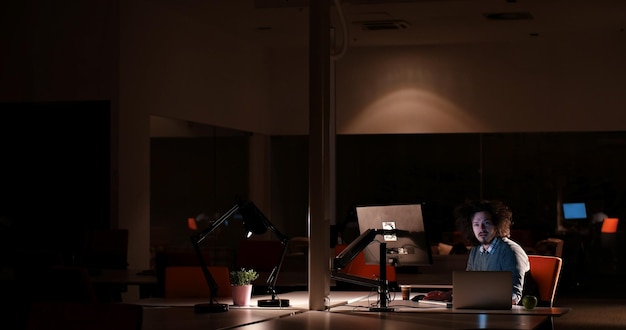 Foto giovane che lavora al computer di notte in un ufficio buio. il designer lavora in un secondo momento.