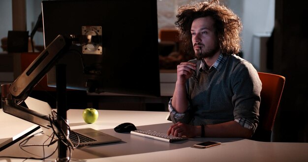 暗いオフィスで夜にコンピューターで作業している若い男。デザイナーは後で働きます。