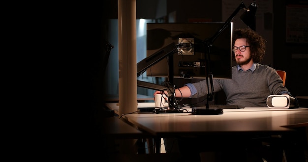 Young man working on computer at night in dark office. the\
designer works in the later time.