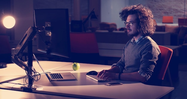 Young man working on computer at night in dark office. the\
designer works in the later time.