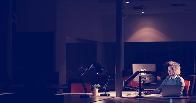 Young man working on computer at night in dark office. The designer works in the later time.