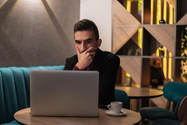 Молодой человек работает на ноутбуке в своем офисе ночью