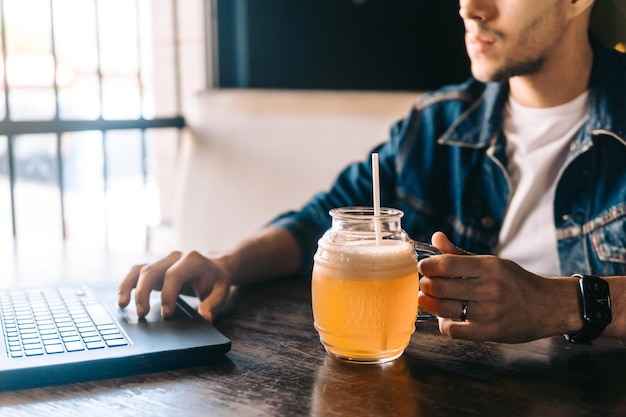 Giovane che lavora su un computer portatile e tiene in mano un bicchiere di birra da una pinta