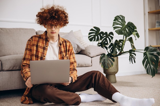 Photo young man working on laptop at home sitting bu the sofa