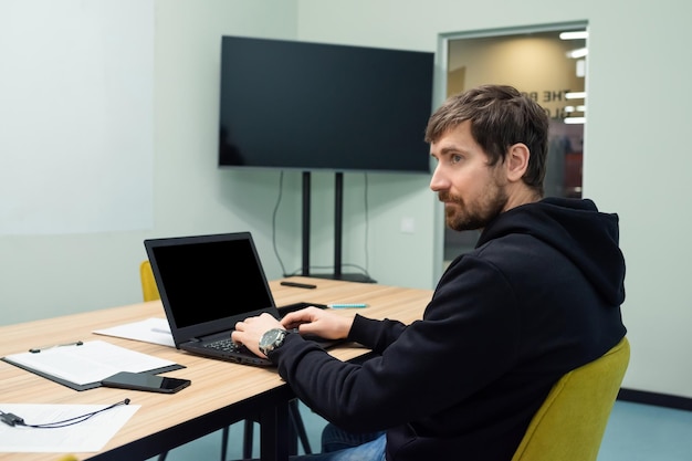 Young man working on laptop sitting at his workplace in coworking office Side view