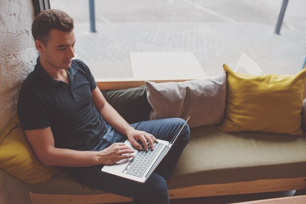 Young man working on laptop while sitting in comfortable couch