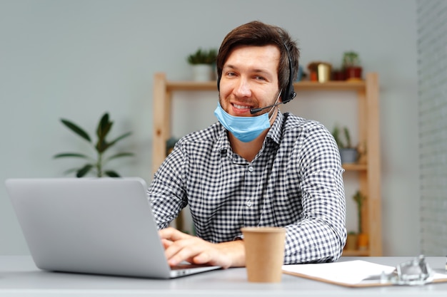 Photo young man working on laptop with headset and face mask at home close up