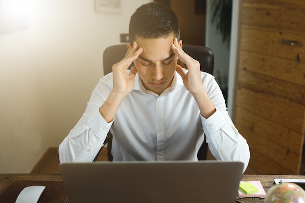 Young man working in office at computer desk. with closed eyes and head in hands. stressed, overworking concept.