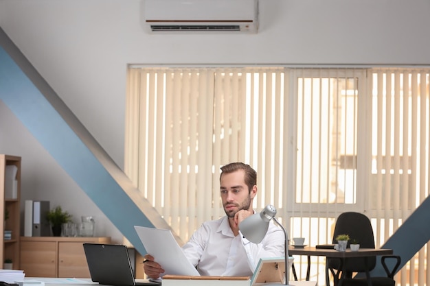 Young man working in office with operating air conditioner