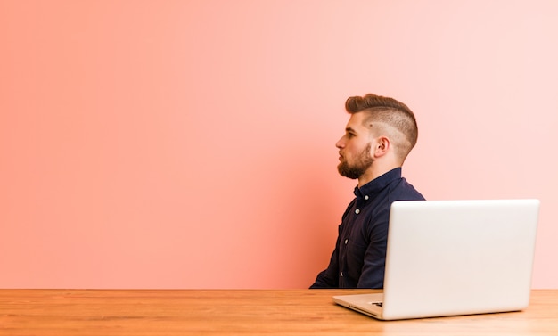 Young man working with his laptop gazing left, sideways pose.