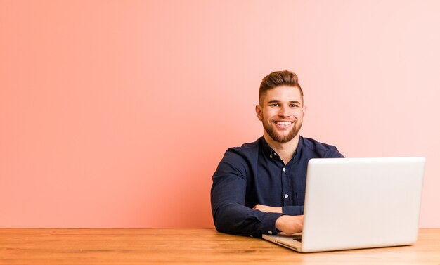Фото Молодой человек, работающий с его ноутбуком, счастливым, улыбающимся и веселым